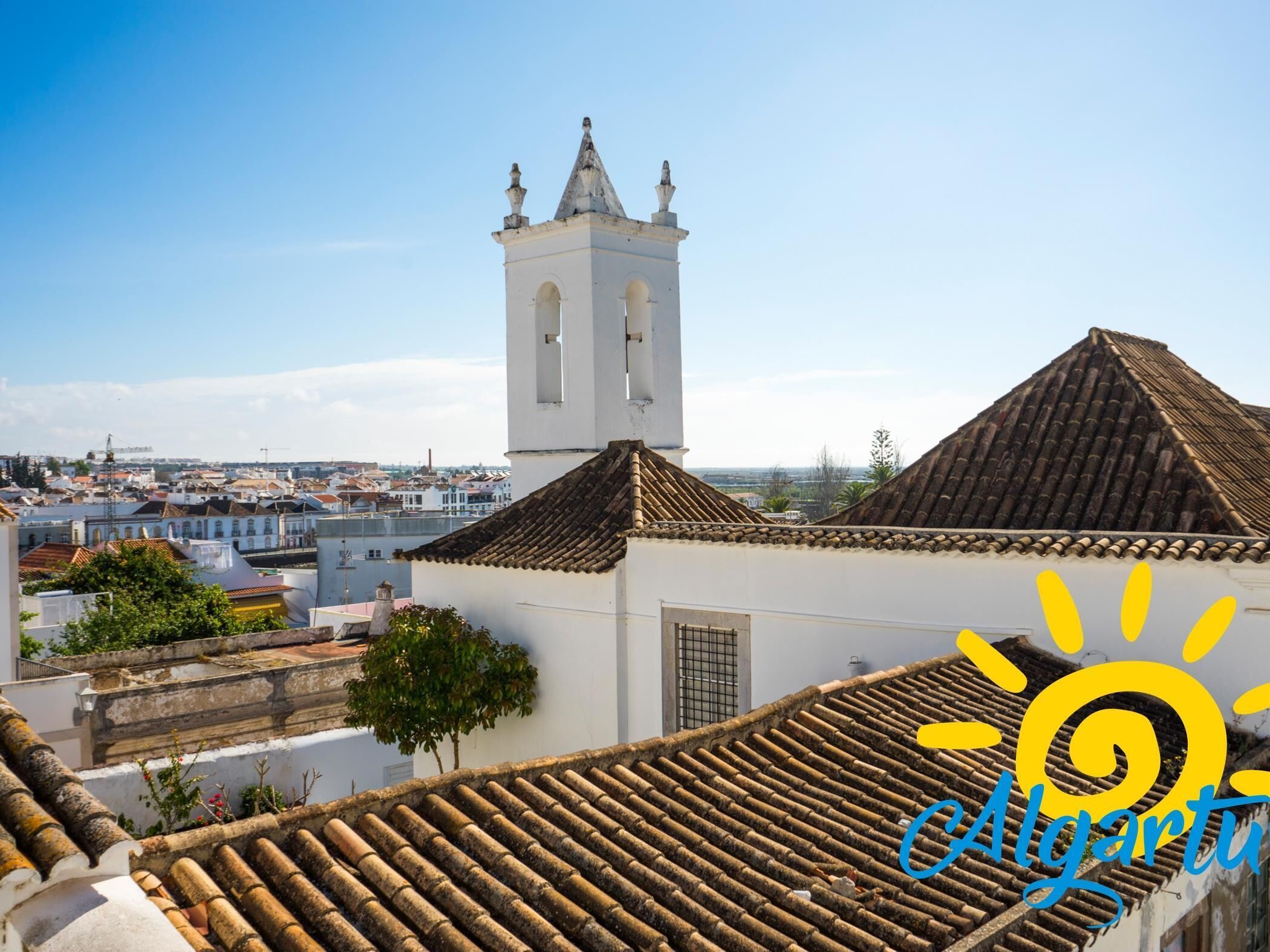 A white building with a bell tower, terracotta roof tiles, and a view of a cityscape.