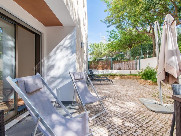 Un patio con dos sillones de descanso y una mesa, una sombrilla y suelo de baldosas de piedra.