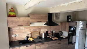 A modern kitchen with wooden cabinetry, a black range hood, a built-in oven, a coffee maker, and a refrigerator.
