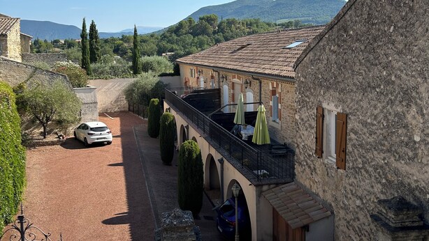 A courtyard with a stone building, a white car, and a mountain in the background.
