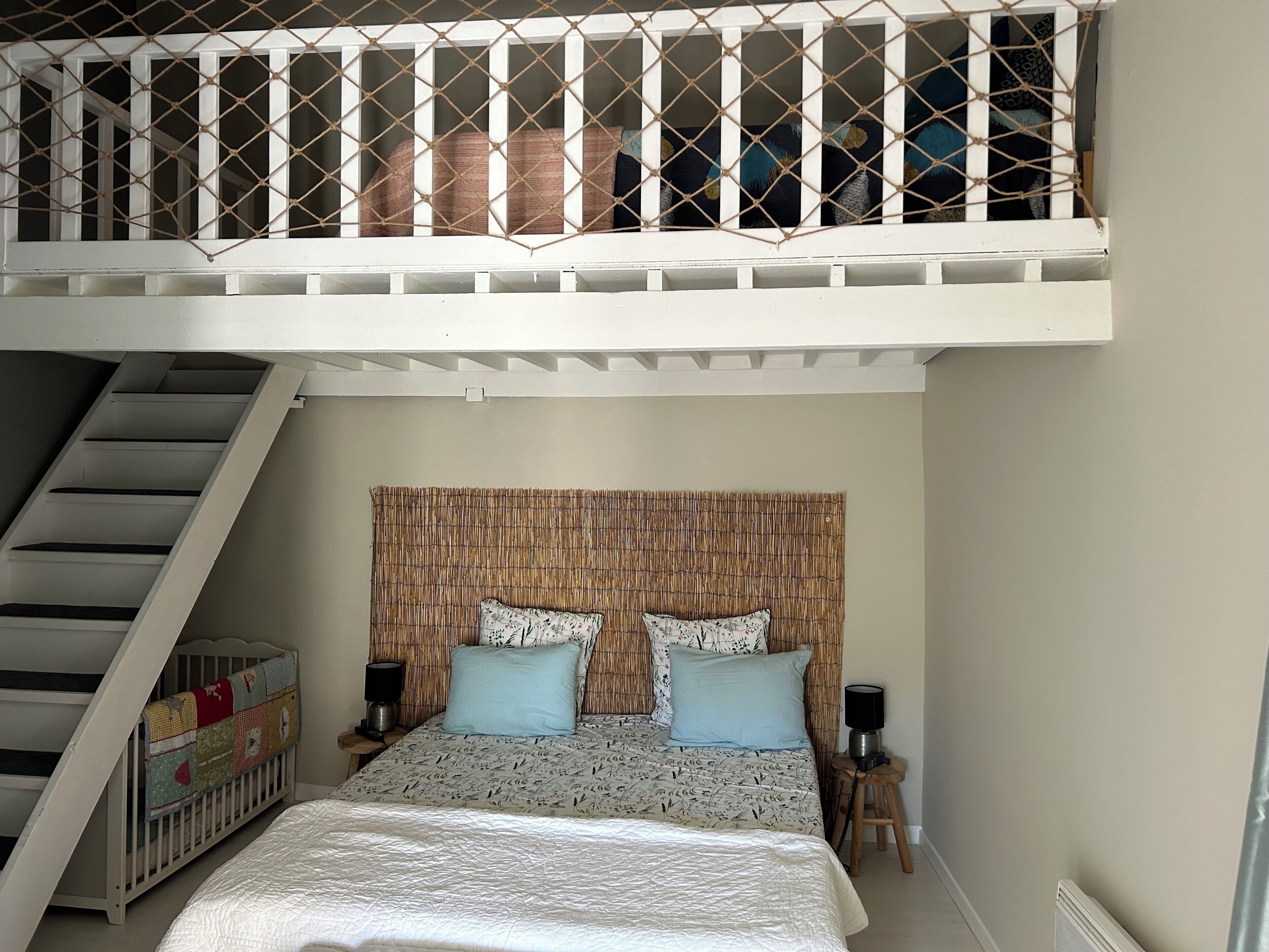 A bedroom with a bunk bed, a headboard with a woven texture, two bedside tables with lamps, and a crib.