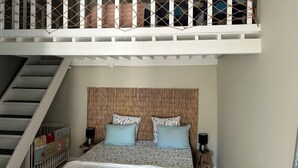 A bedroom with a bunk bed, a headboard with a woven texture, two bedside tables with lamps, and a crib.