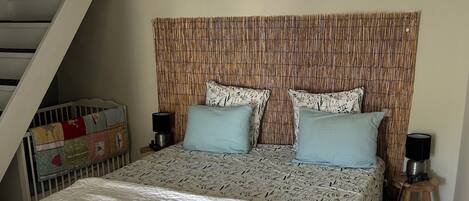 A bedroom with a large bed, a bench, a staircase, and a headboard with a woven pattern.
