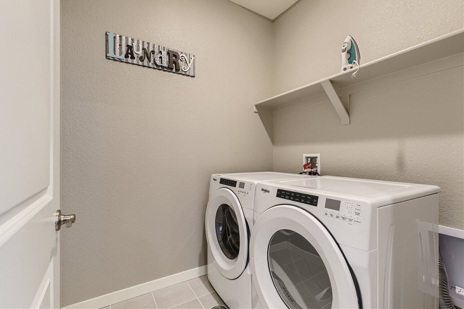 A laundry room with two front-loading washing machines, a metal sign above the machines, and a shelf above the right machine.