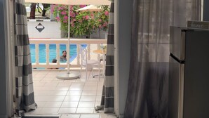 A room with a view of an outdoor pool area, a door with a striped curtain, and a refrigerator. - Poolside Suites 5-Mins from the Beach w/ AC & Wi-Fi (Rodney Bay)