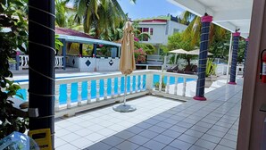 A pool area with a tiled floor, a pool with a blue and white color scheme, and a covered seating area with umbrellas. - Poolside Suites 5-Mins from the Beach w/ AC & Wi-Fi (Rodney Bay)