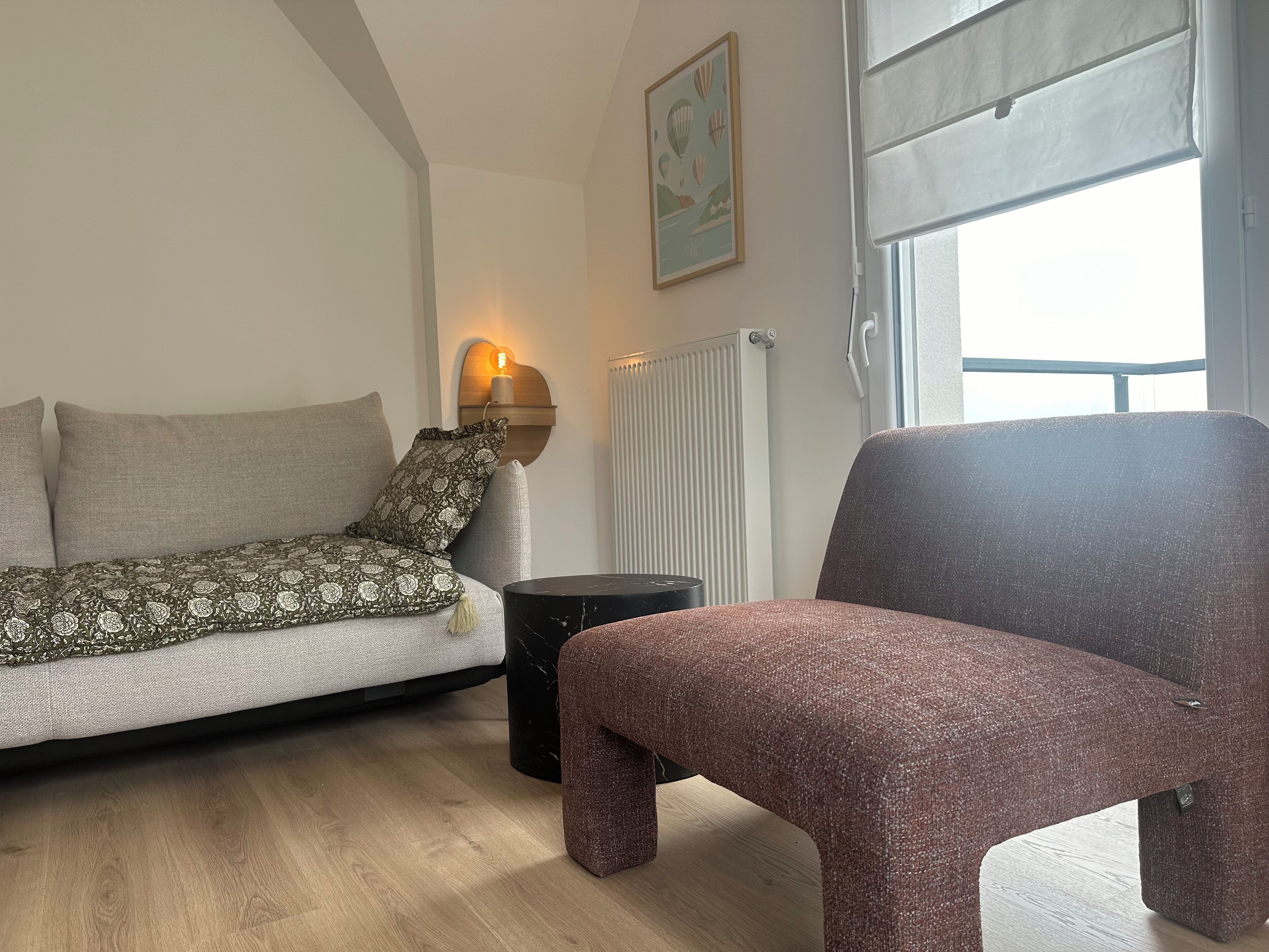 Un salon moderne avec un canapé, un plaid à motifs, une petite table d’appoint et une grande fenêtre donnant sur un beau paysage.
