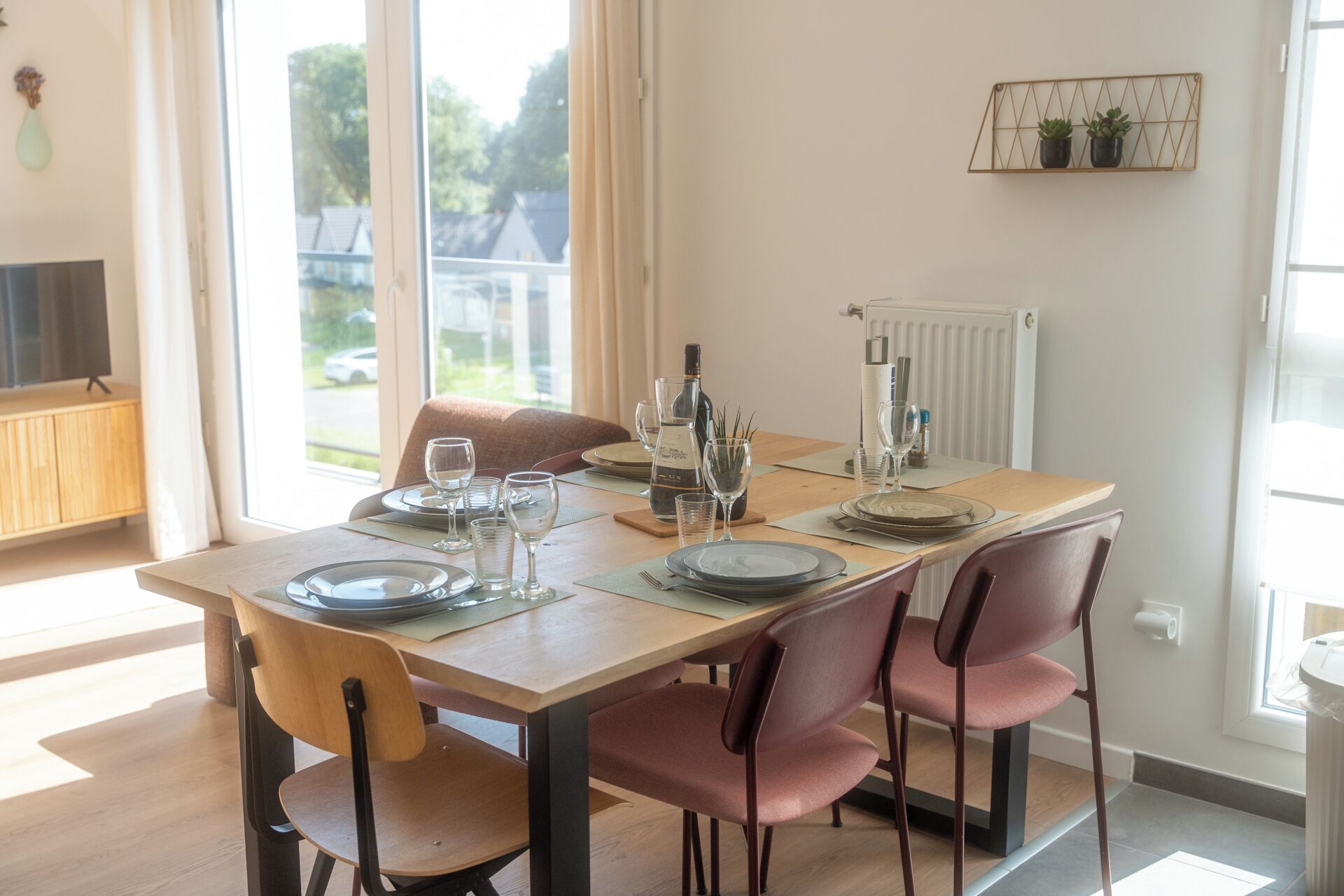 A dining area with a wooden table set for four, equipped with plates, glasses, and a wine bottle.