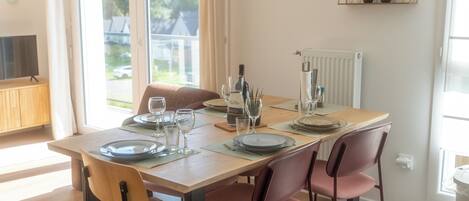 A dining area with a wooden table set for four, equipped with plates, glasses, and a wine bottle.