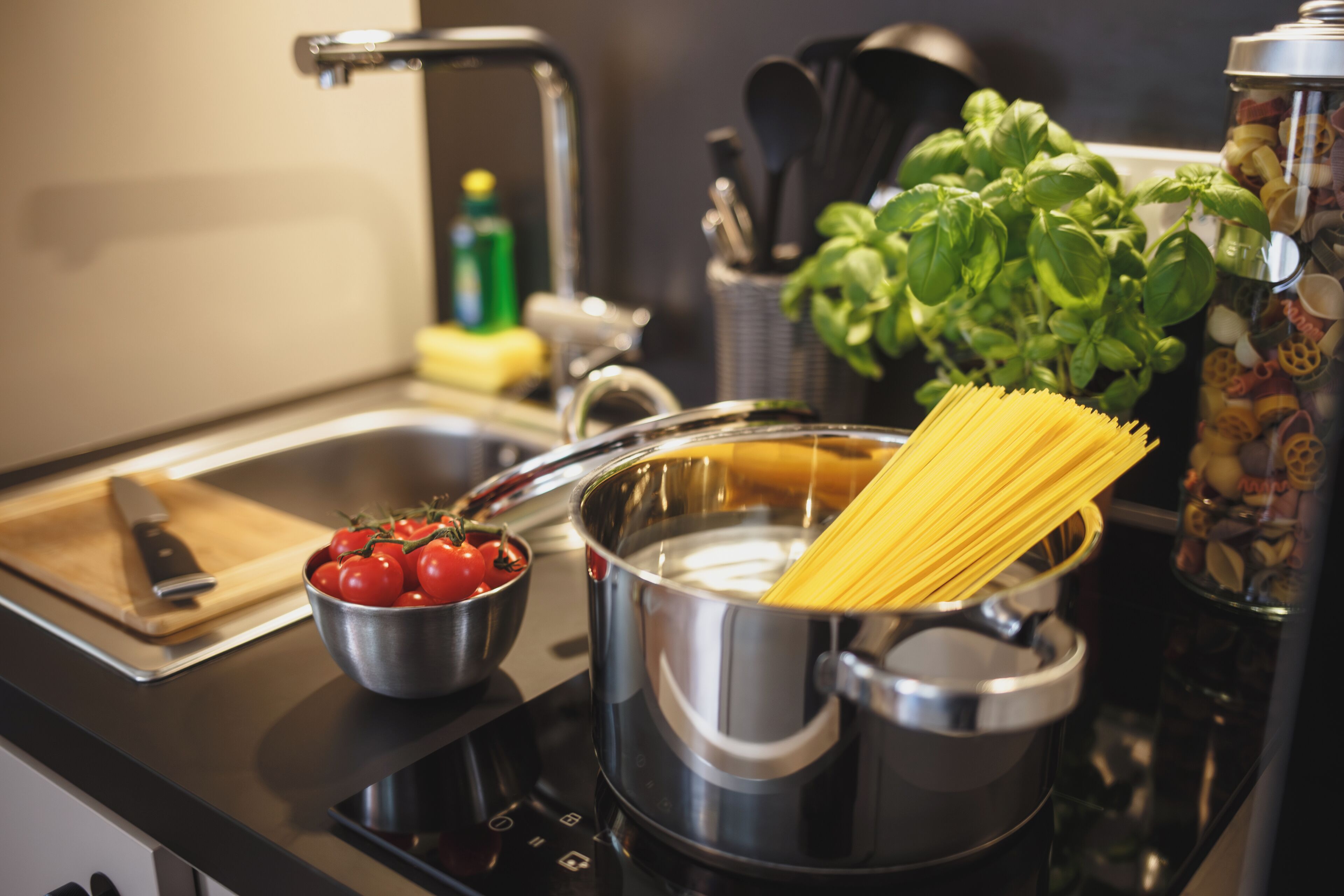 A kitchen with a pot of boiling water, a bowl of tomatoes, and a cutting board with a knife.