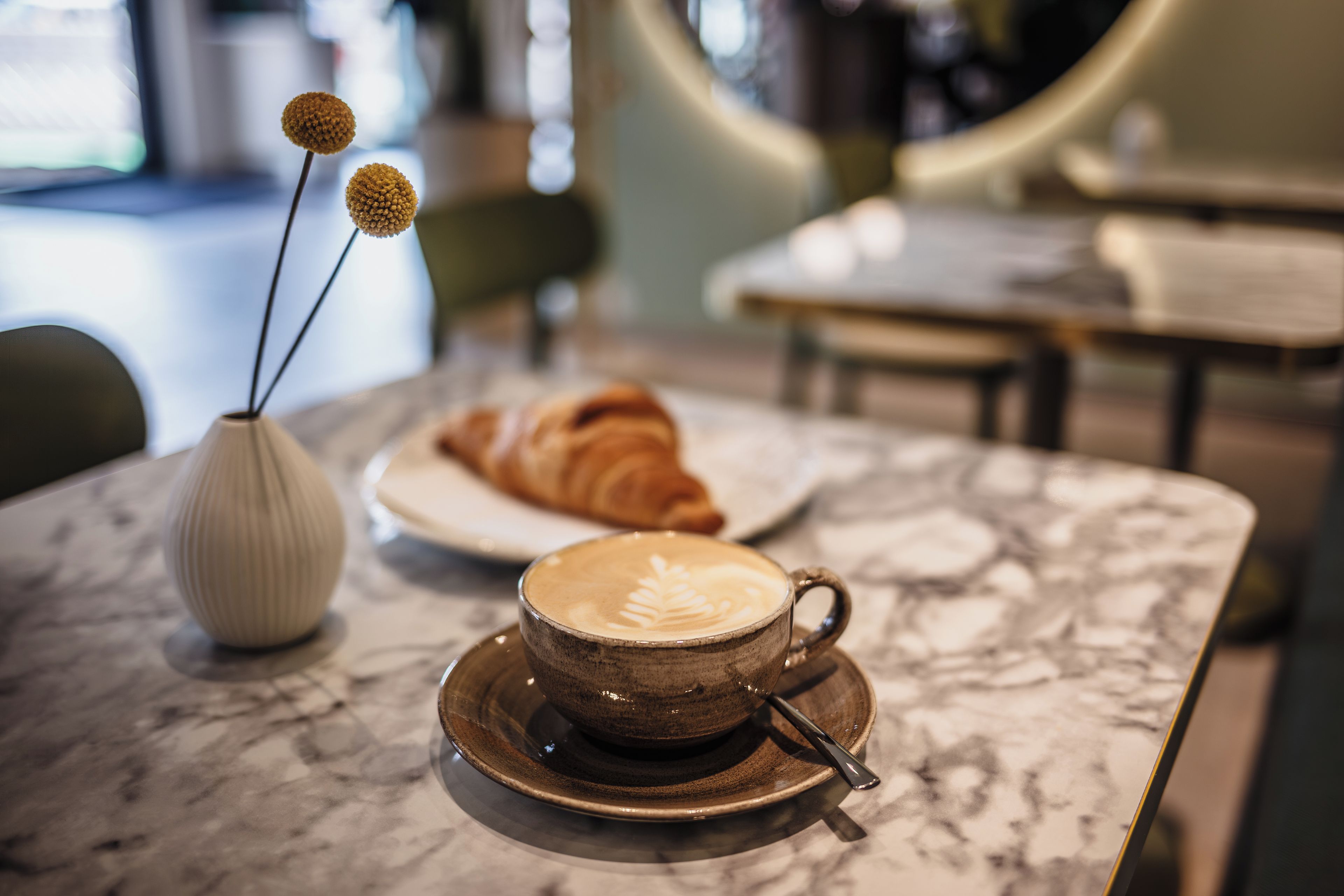 A marble table with a cup of coffee and a croissant.