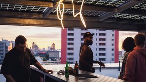 A rooftop bar with a city view, a neon sign, and a bartender. - The Circus Living (Berlin)