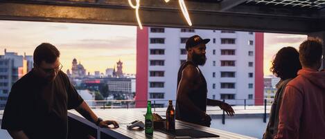 A rooftop bar with a city view, a neon sign, and a bartender.