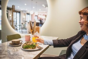 A person sitting at a table with a plate of food, a drink, and a cup. - The Circus Living (Berlin)