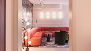 A modern lounge area with a curved red sofa, a round table, and a green ottoman. - The Circus Living (Berlin)