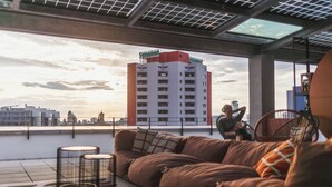 A modern interior with a sofa and two floor lamps, a large window with a view of a building and the sky. - The Circus Living (Berlin)
