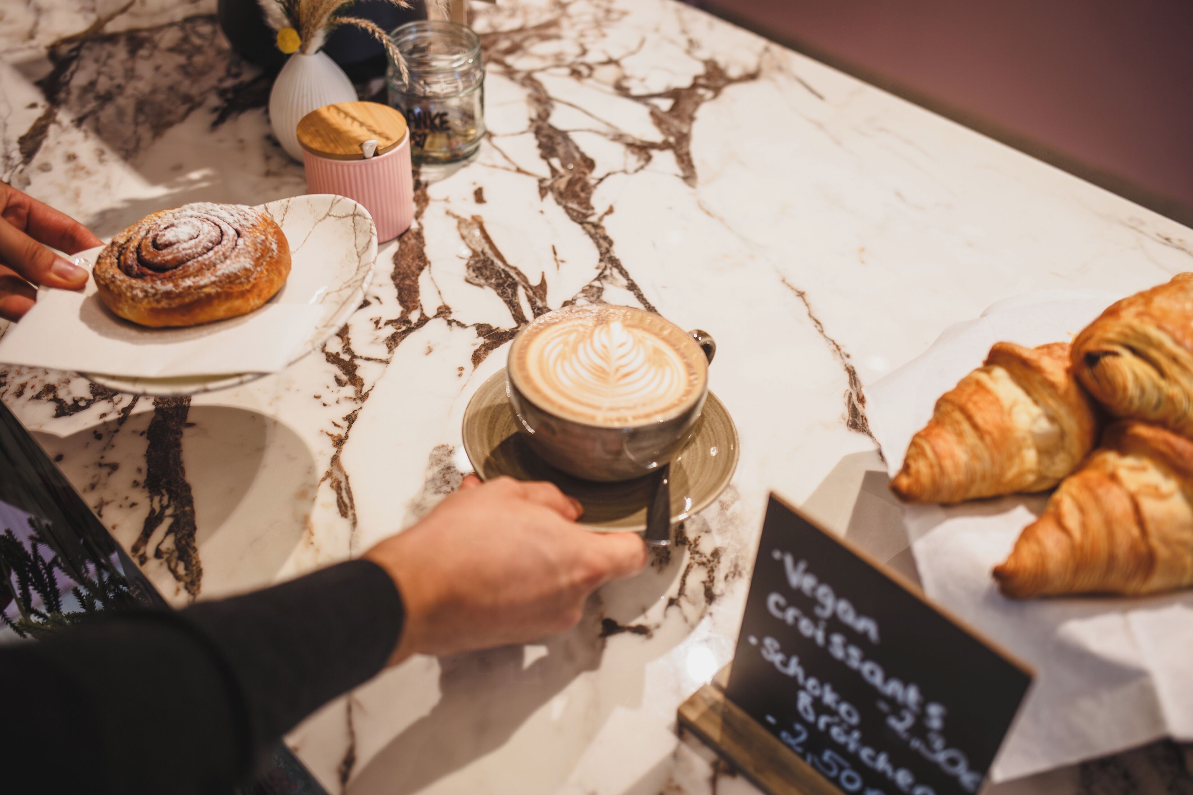 A table with pastries, a coffee cup, and a sign indicating vegan croissants.
