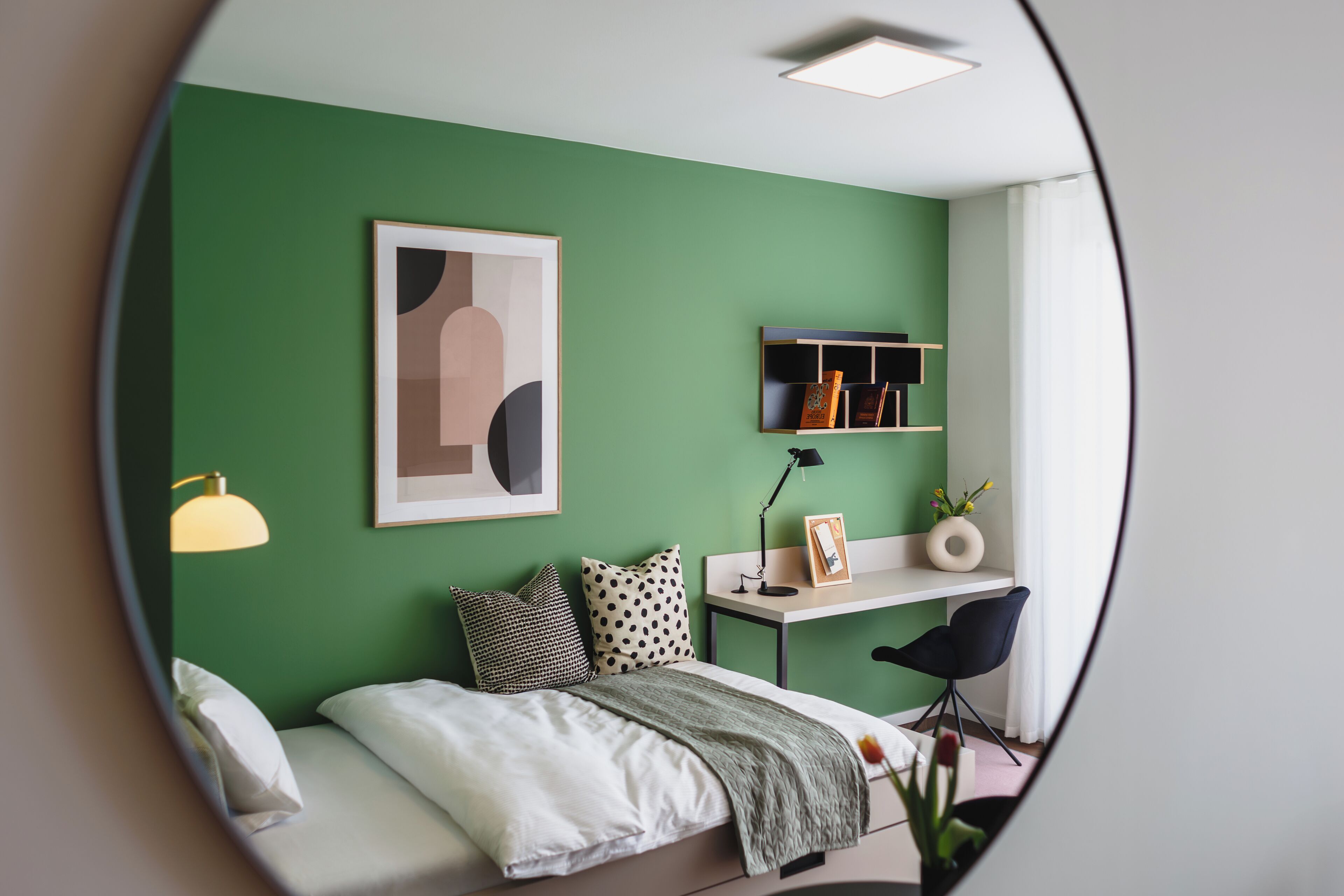 A room with a bed, a desk, a chair, a shelf with books, and a framed picture on the wall.