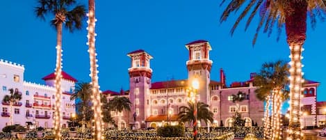 A grand hotel with a central tower, surrounded by well-lit palm trees and manicured gardens.