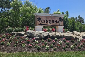 A sign with the name 'COQUINA' and the number '7900' in a landscaped area with rocks and flowers.