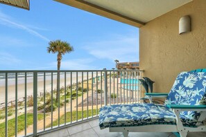 A balcony with a view of the beach, a pool, and a palm tree.