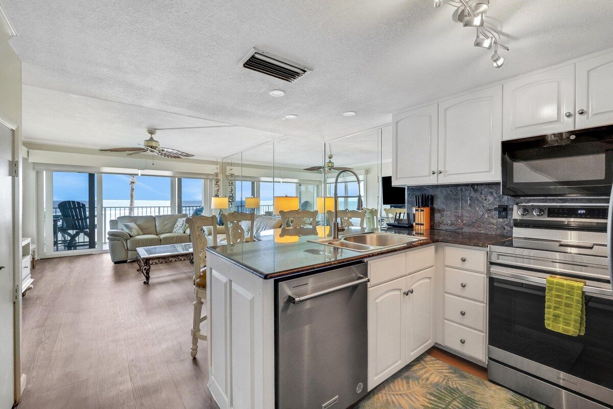 A modern kitchen with a dishwasher, oven, and a large window overlooking a balcony.