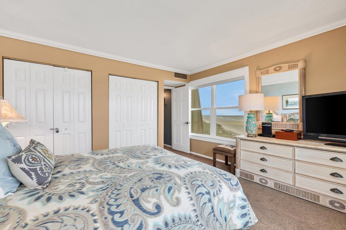 Een slaapkamer met een bed, een dressoir, een televisie en een raam met uitzicht.