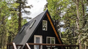 Eine Holzhütte mit einer Holzterrasse und einer Treppe zu einem Balkon, umgeben von Bäumen.