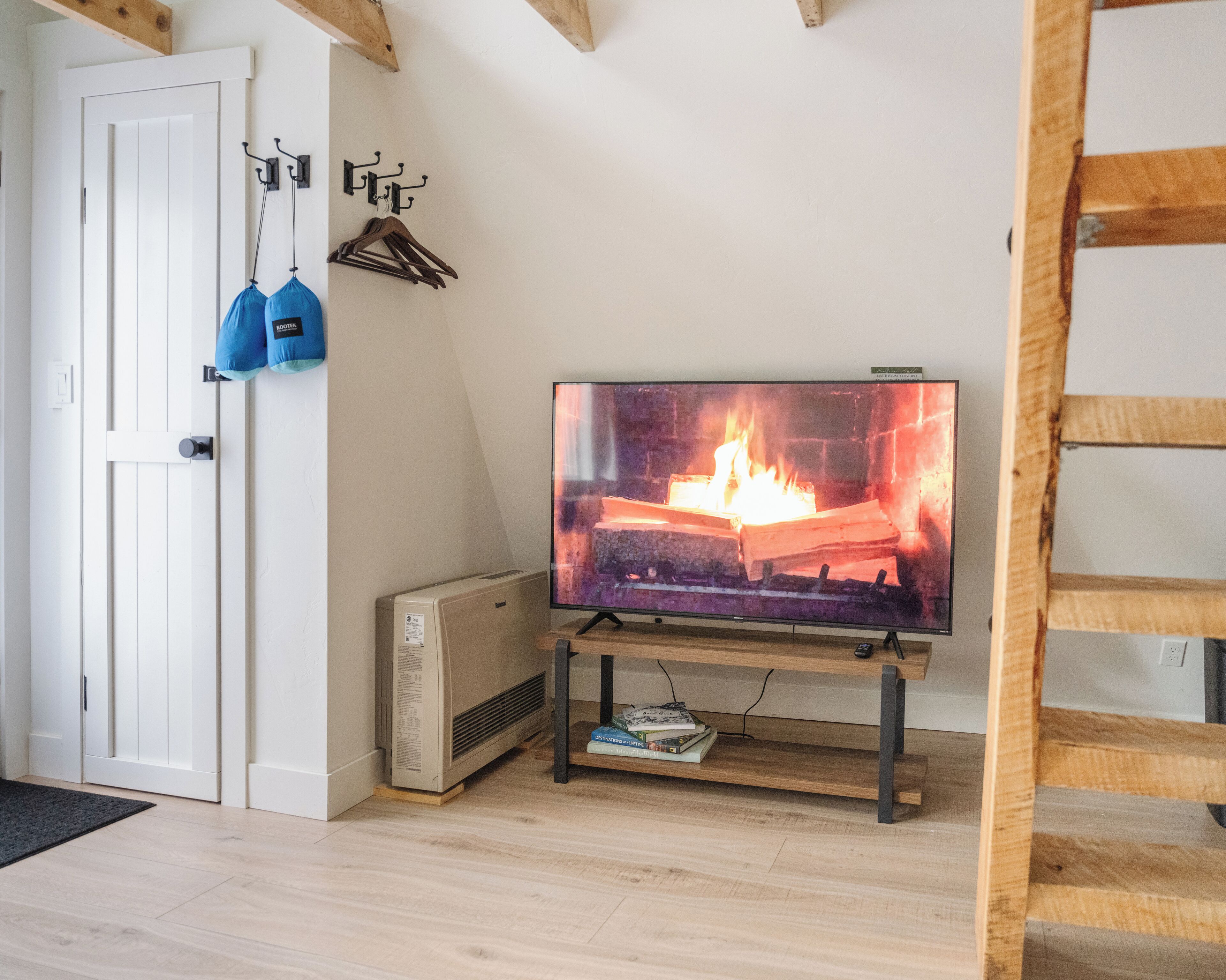 Una sala de estar con una televisión mostrando una chimenea, una puerta blanca y una escalera de madera.