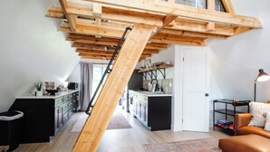 Ein Loft-Wohnraum mit Holztreppe, einer Küchenzeile und einer Sitzecke mit Teppich.