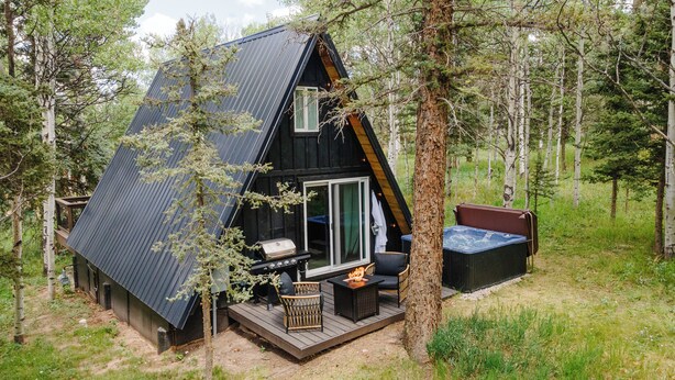 Eine Hütte mit geneigtem Dach, einer Sitzterrasse, einem Grill und einem Whirlpool.
