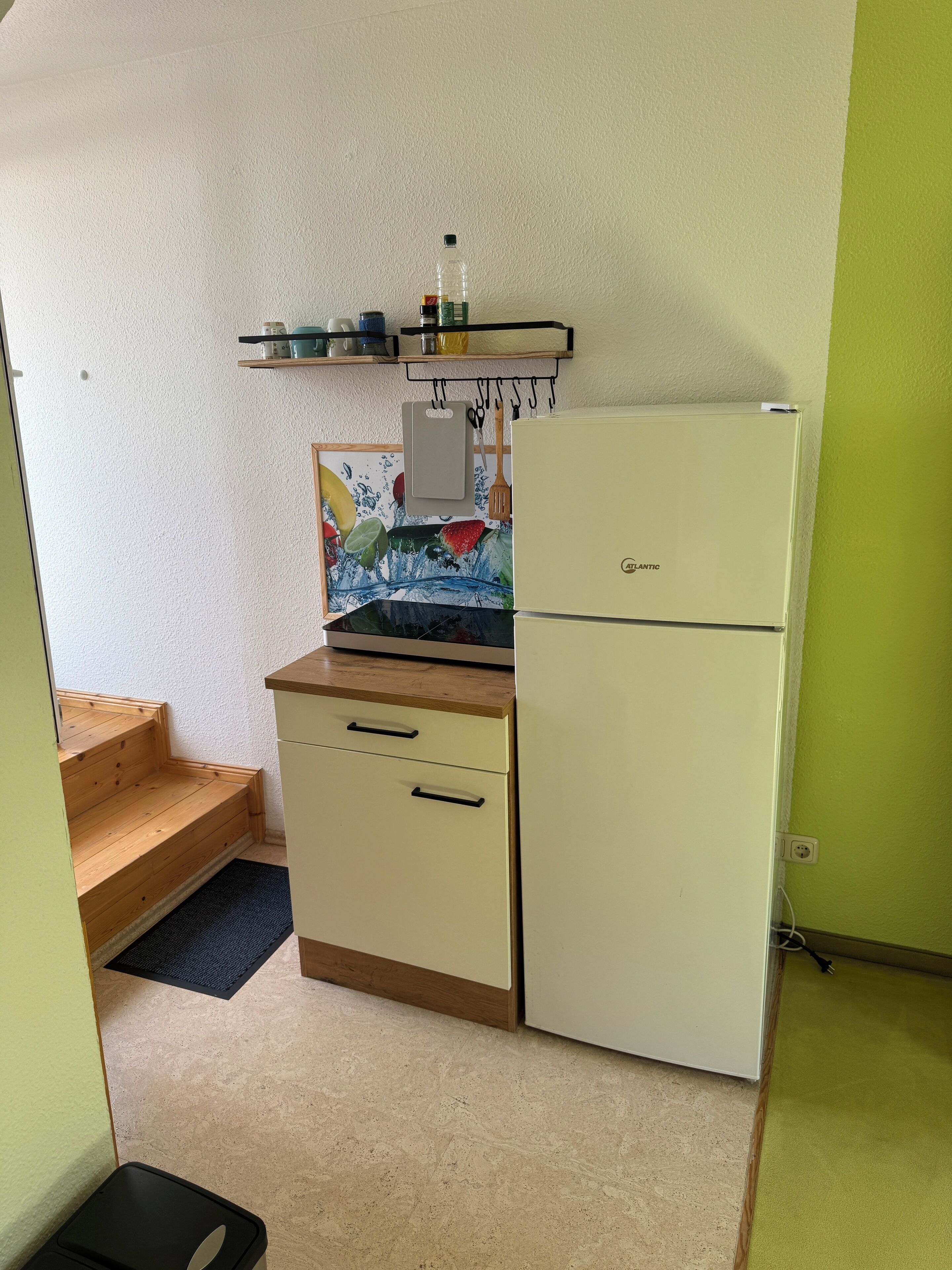 Une petite cuisine équipée comprenant un réfrigérateur, un plan de travail en bois et une petite étagère contenant des ustensiles de cuisine.