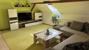 A modern living room with a sloped ceiling, a flat-screen TV, a sofa, a coffee table, and a potted plant. - Loft mit Privater Dachterrasse (Gera)