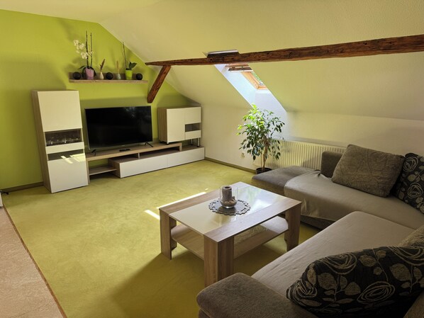 Un salon moderne avec un plafond en pente, un téléviseur à écran plat, un canapé, une table basse et une plante en pot.