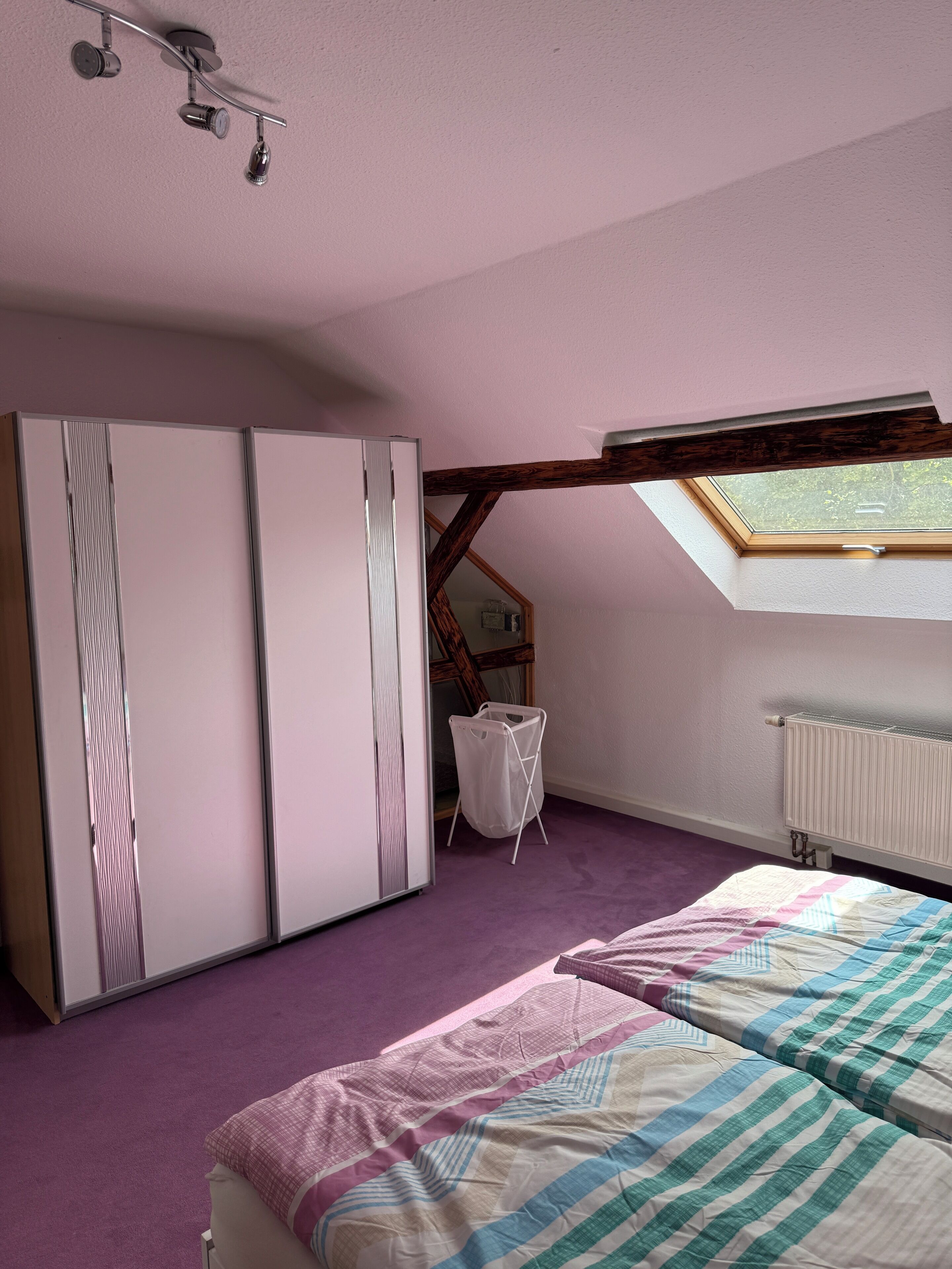 Un dormitorio con cama, armario, tragaluz y radiador.