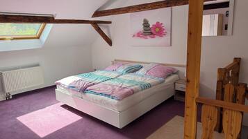 Ein Schlafzimmer mit Bett, Fenster, Heizkörper und einem Holzbalken an der Decke.