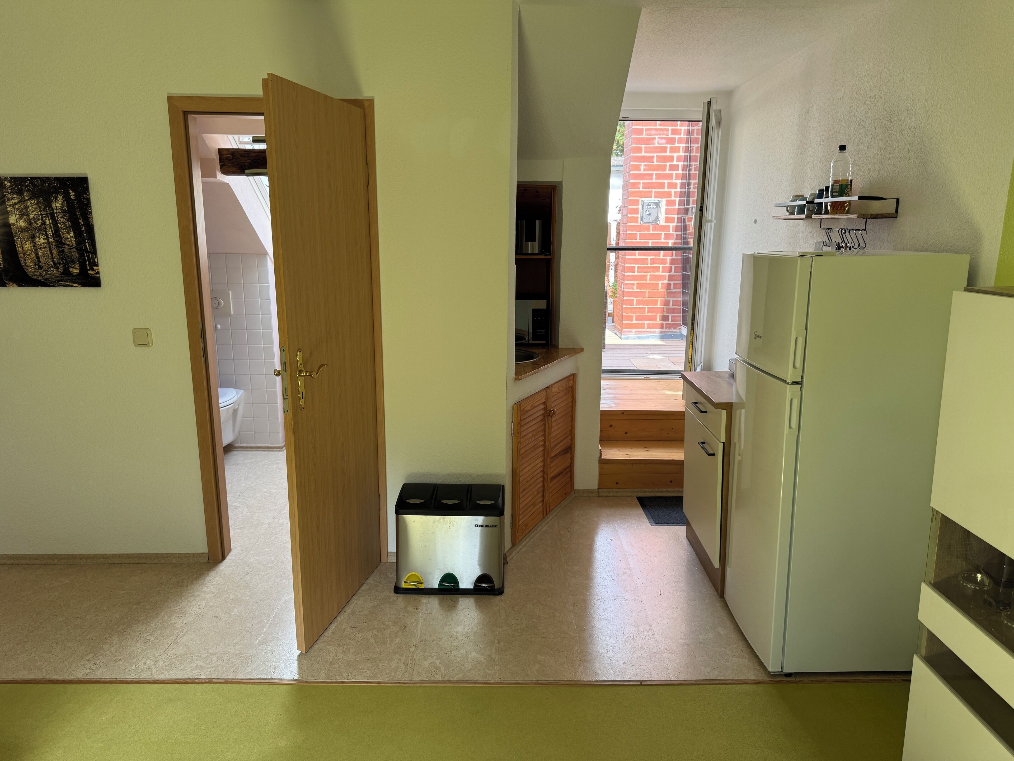 Een compacte keuken met een koelkast, een wastafel en een raam met uitzicht op een gebouw van baksteen.