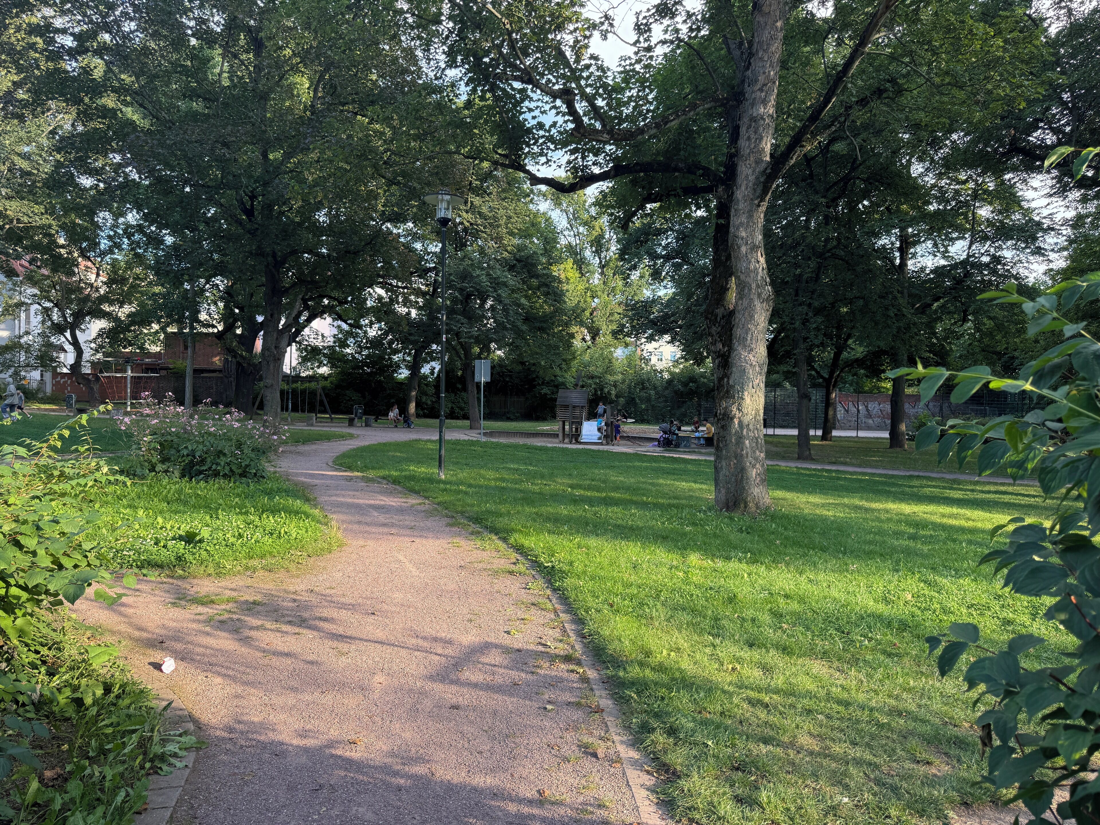 Um parque com um caminho pavimentado, grama verde e árvores.