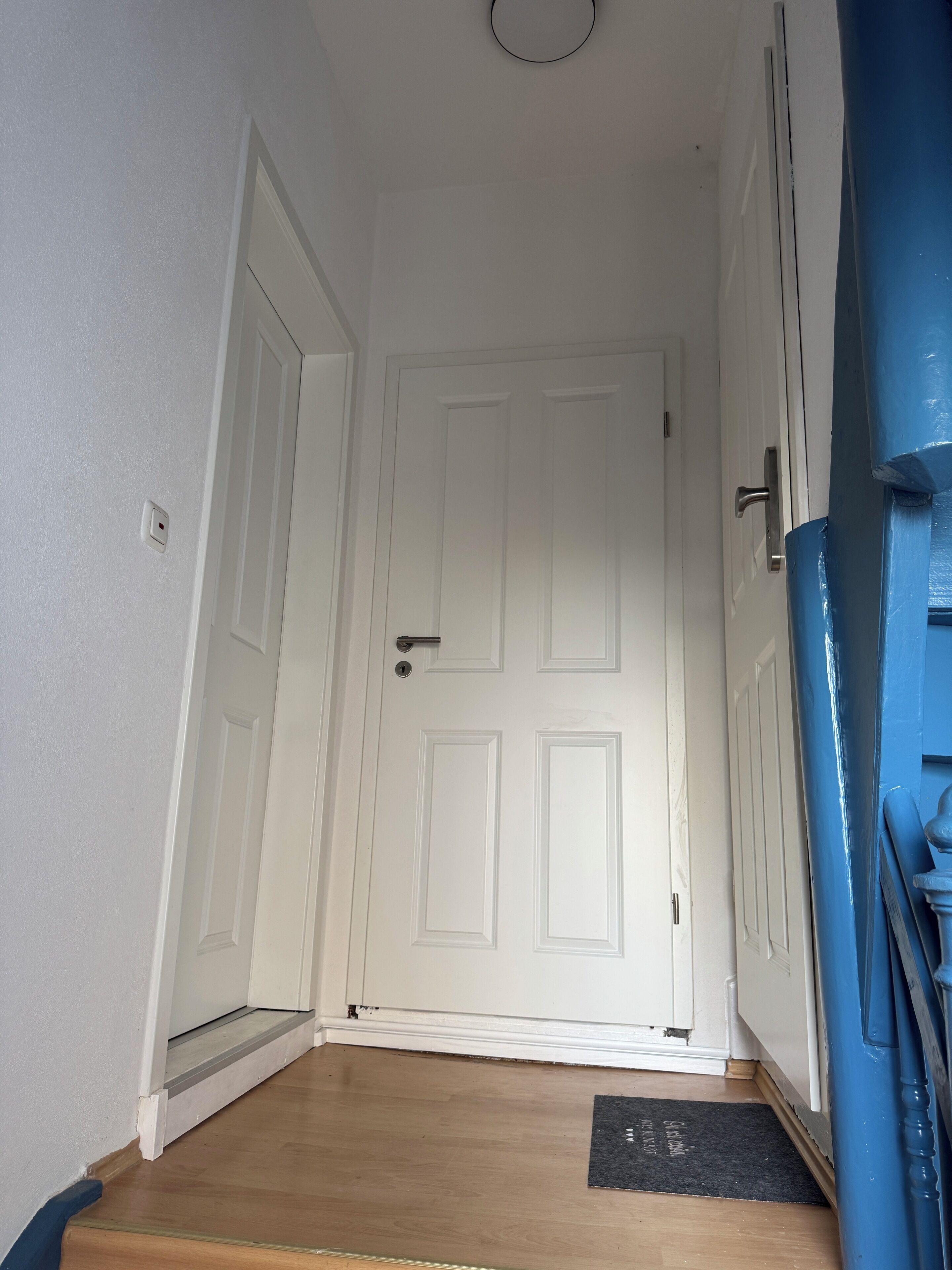 A hallway with a white door, a wooden floor, and a blue wall.