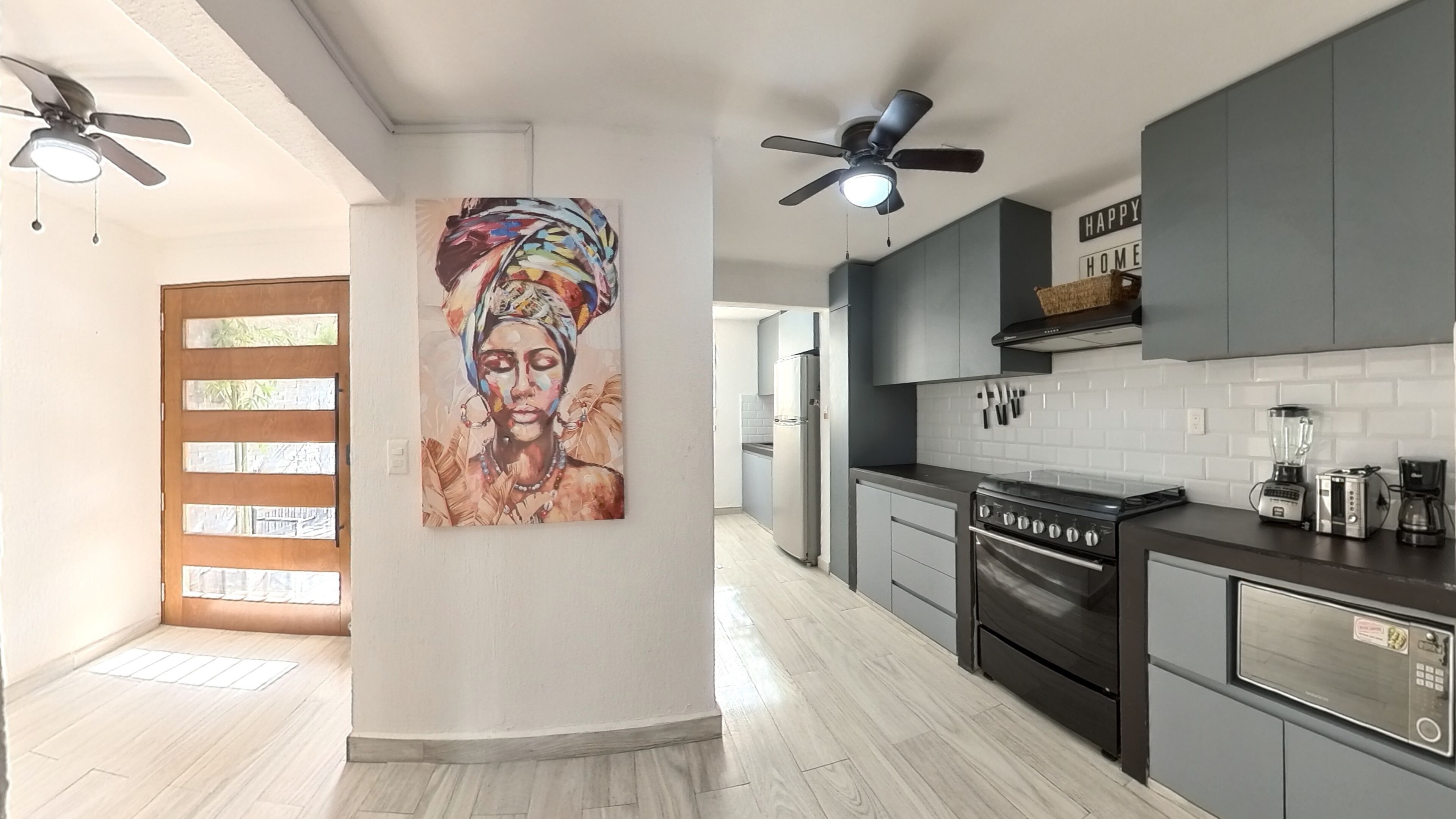 A modern kitchen with grey cabinets, a black stove, and a microwave. There is a painting on the wall and a ceiling fan.