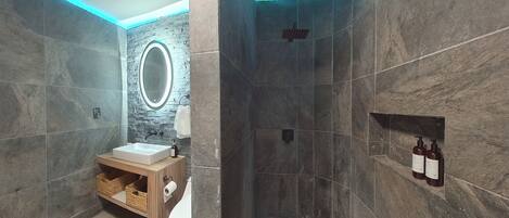 A modern bathroom with a stone wall, a wooden vanity, a sink, a toilet, and a shower area.