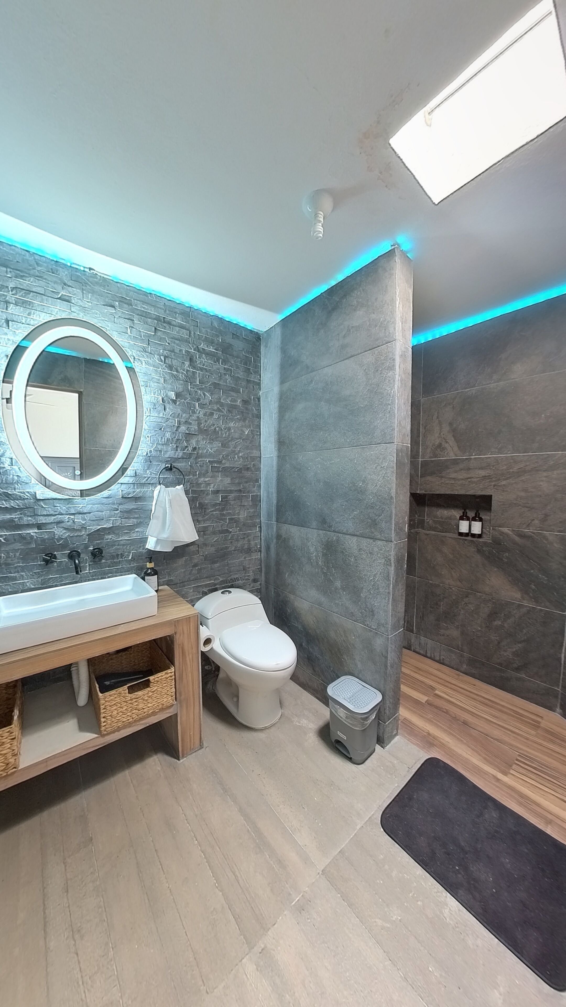 A modern bathroom with a stone wall, a round mirror, a toilet, and a sink.