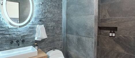 A modern bathroom with a stone wall, a round mirror, a toilet, and a sink.