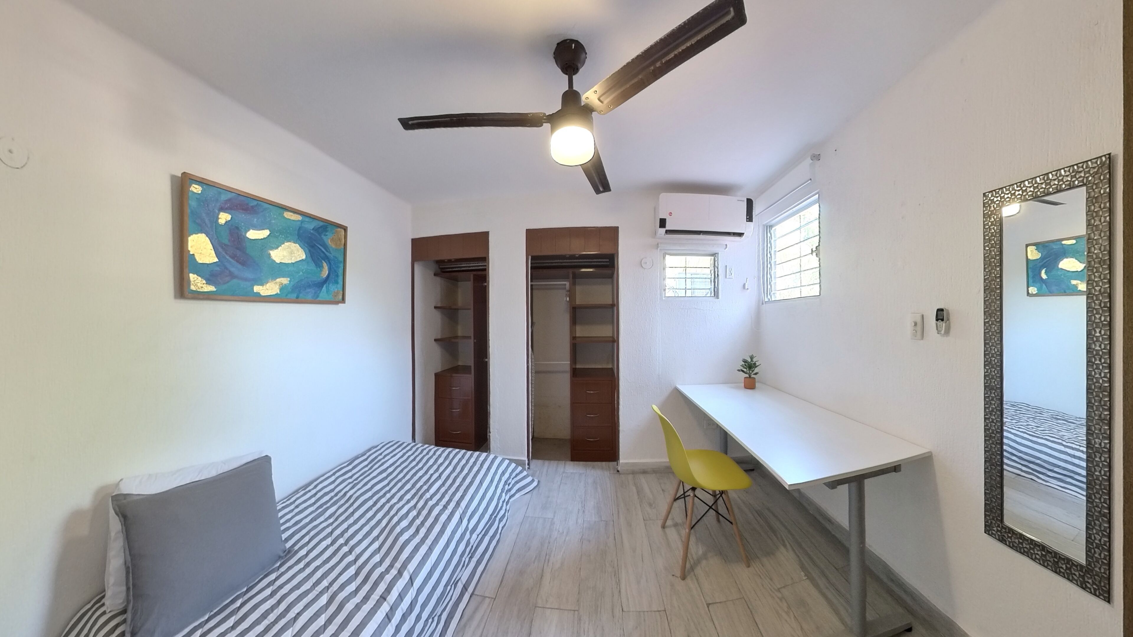 Quarto com cama, escrivaninha, cadeira, ventoinha no teto e guarda-roupa.