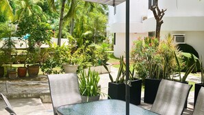 An outdoor patio with a glass-top table and chairs, surrounded by potted plants and a white umbrella. - Casa Comfy (Cancun)