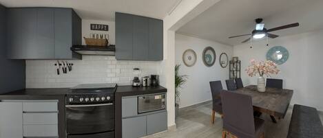 A modern kitchen with grey cabinets, a built-in oven, and a dining area with a wooden table and chairs.