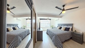 A mirrored bedroom with two beds, ceiling fans, a window, and a desk. - Casa Comfy (Cancun)