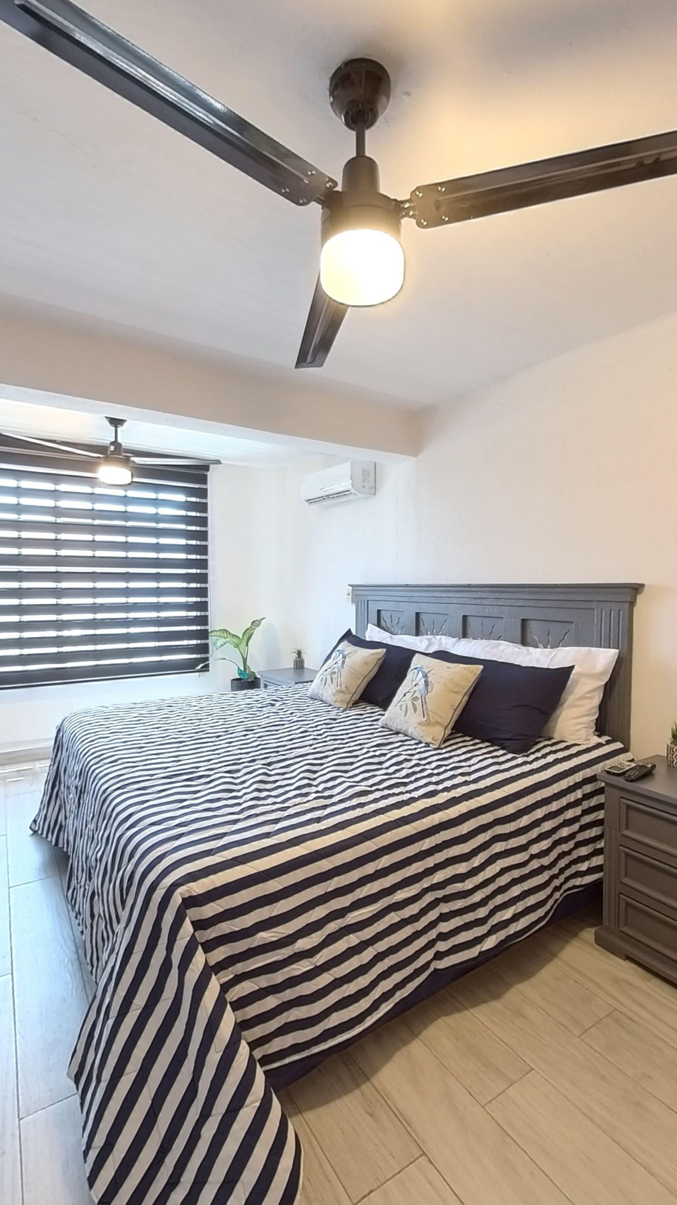 A bedroom with a bed, a nightstand, a ceiling fan, and a window with blinds.