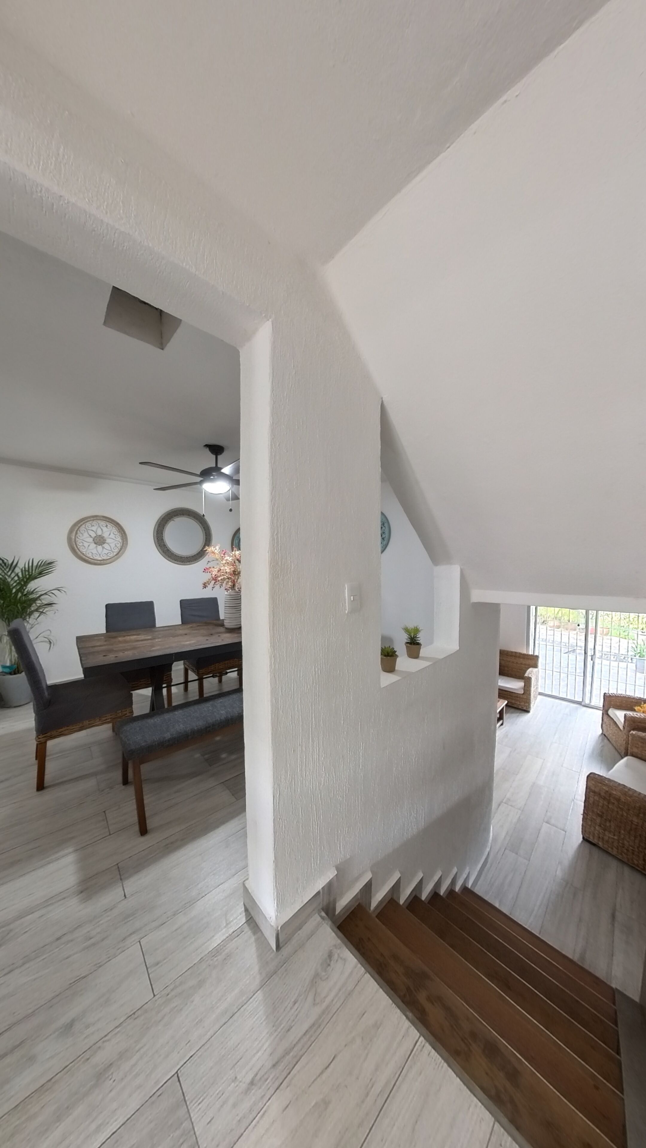 A spacious living area with a dining table, chairs, and a bench. There is a staircase leading to an upper level.