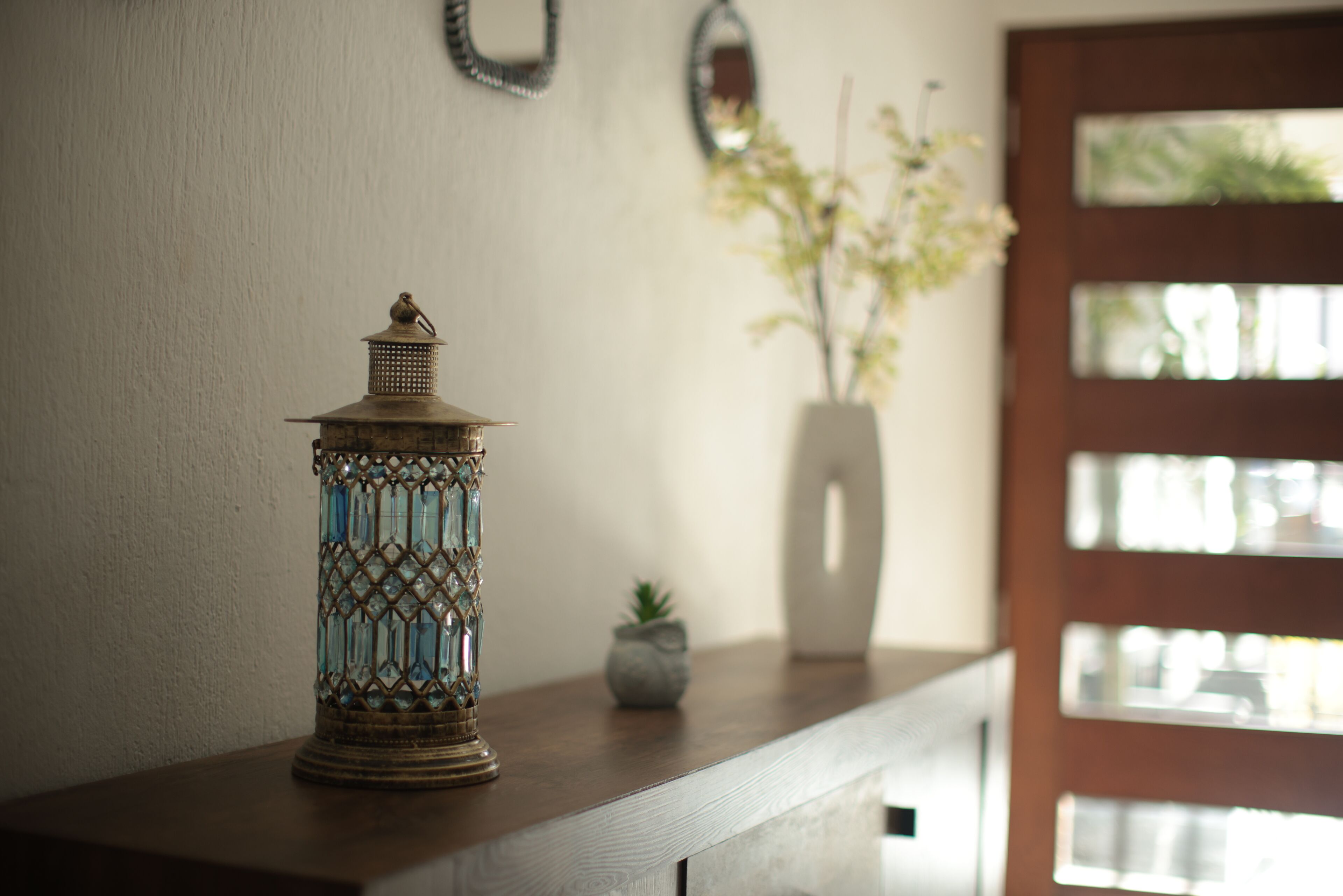 A decorative glass vase on a wooden surface, a small potted plant, and a mirror on the wall.